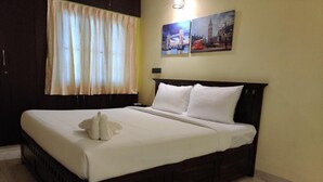 Una cama bien hecha con sábanas y almohadas blancas, un cabecero de madera oscura y una ventana con cortinas translúcidas.