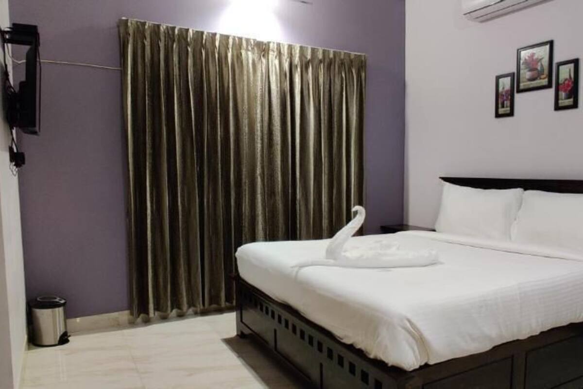 Habitación de hotel con cama, cortinas, un cubo de basura y cuadros en la pared.