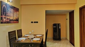 Un comedor con una mesa dispuesta para cuatro, un ventilador de techo, un refrigerador y una lámpara fijada a la pared.