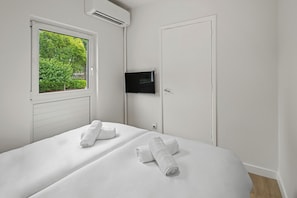 Habitación de hotel con dos camas, un televisor montado en la pared y una ventana con vistas a zonas verdes.