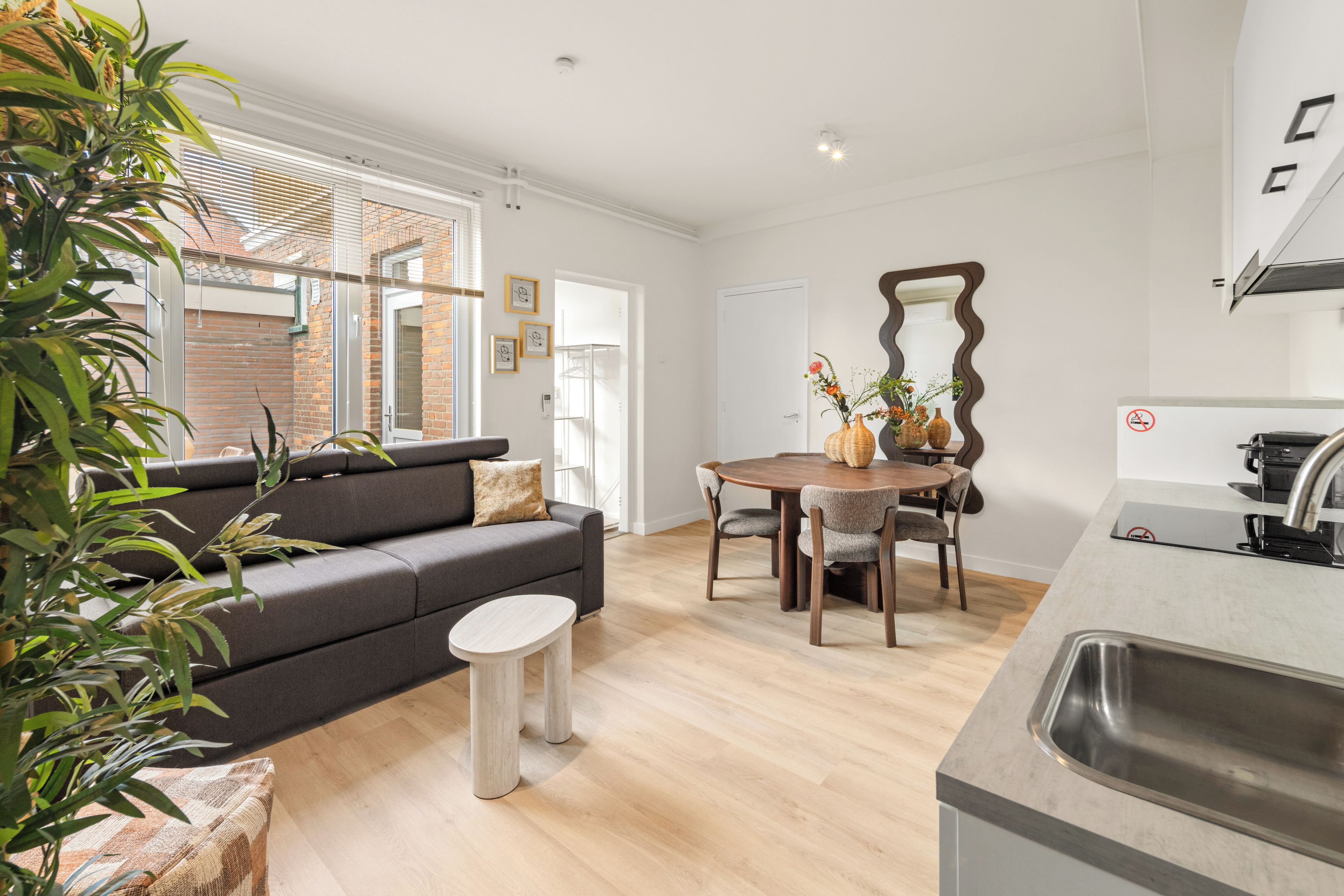En moderne opholdsstue med sofa, spisebord med stole, et køkkenområde og et stort spejl.