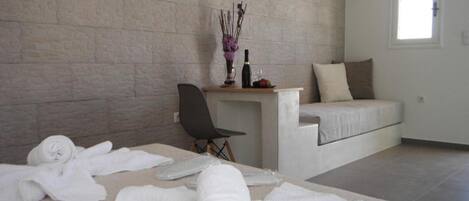 Une chambre moderne avec un mur en briques, un lit, une chaise et une petite table sur laquelle se trouvent un vase et des bouteilles.