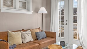Un salon avec un canapé en cuir marron, une table basse en verre, un lampadaire et une porte avec des rideaux.