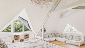 Een slaapkamer met een schuine kap, een bed, een zithoek en een raam.