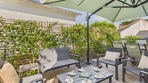 Een terras buiten met houten meubels, een tafel met kopjes en schotels, en een grote parasol.