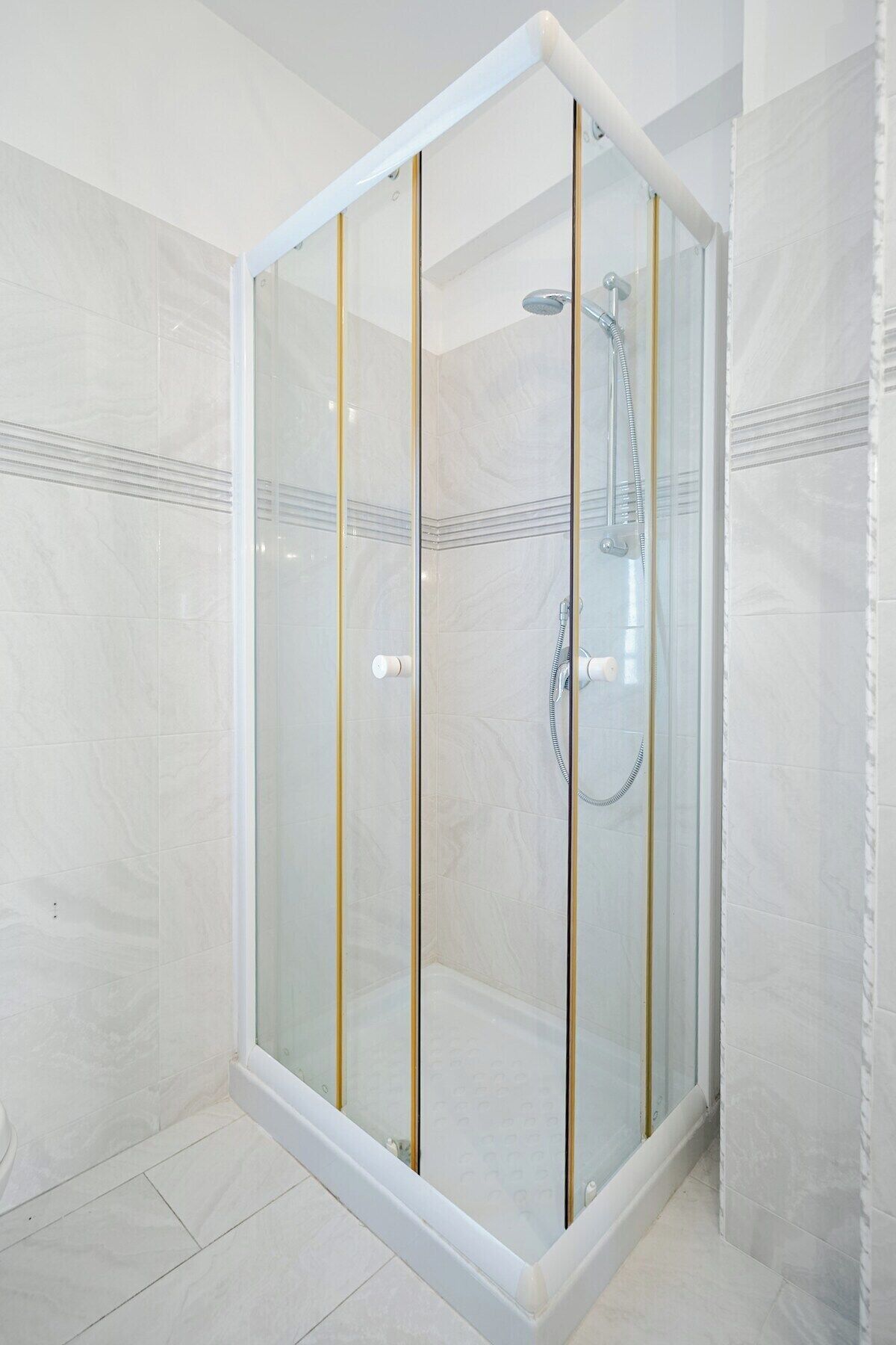 A glass-enclosed shower stall with a handheld showerhead and a wall-mounted faucet.