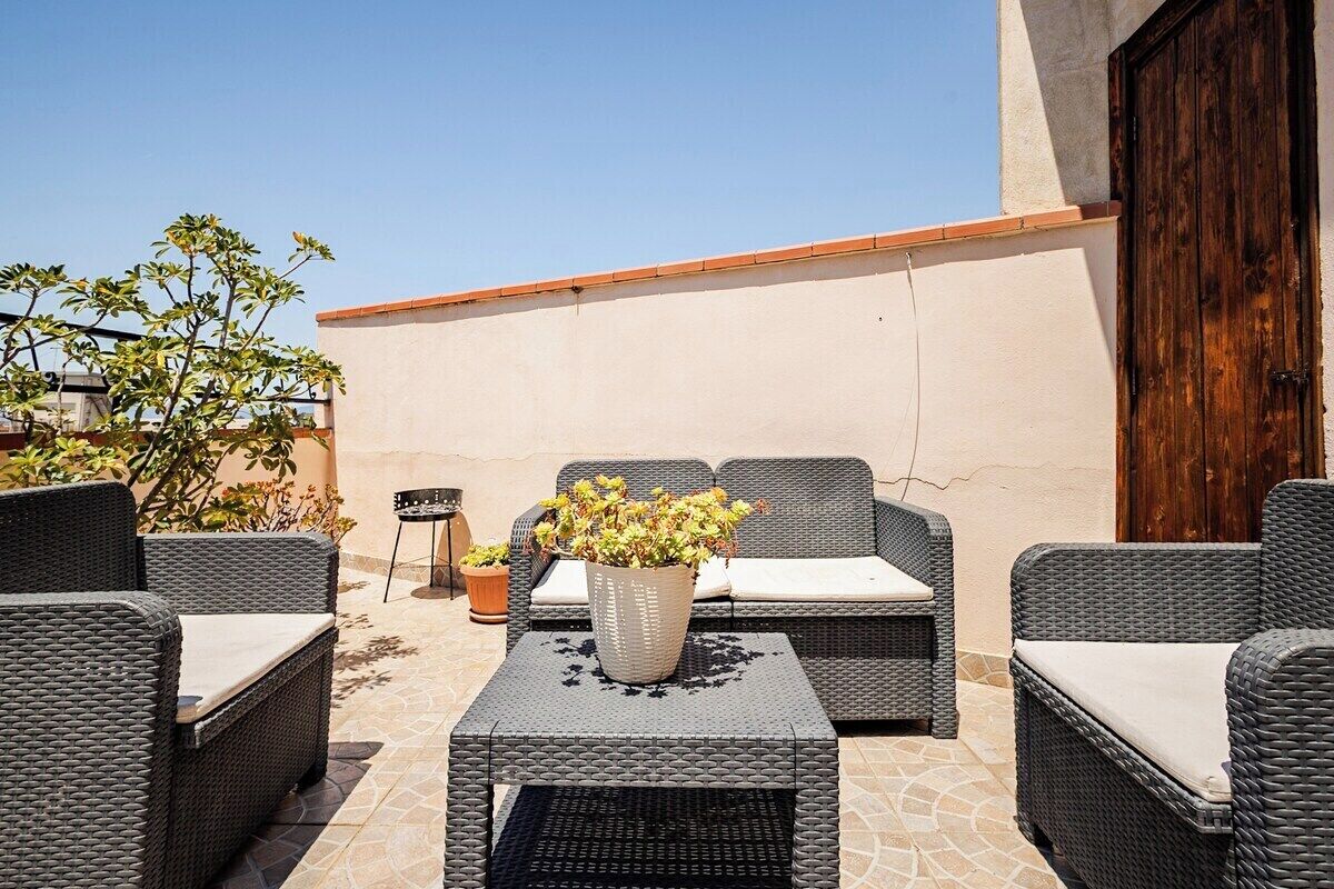 Une terrasse extérieure avec des meubles en osier, une plante en pot et une porte en bois.