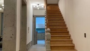 Gradi de fusta en un passadís, amb un llum al sostre i una porta que dona a una altra habitació.