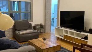 Un saló amb un sofà, una taula de centre, una televisió sobre un suport i una catifa amb dibuixos.