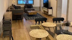 Un saló modern amb una taula de dinar de vidre, sofàs, una televisió i una finestra gran.