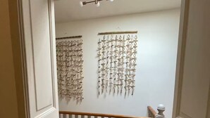 Una escala amb barana de fusta i una barana de protecció, que condueix a una habitació amb una paret blanca i una lluminària al sostre.