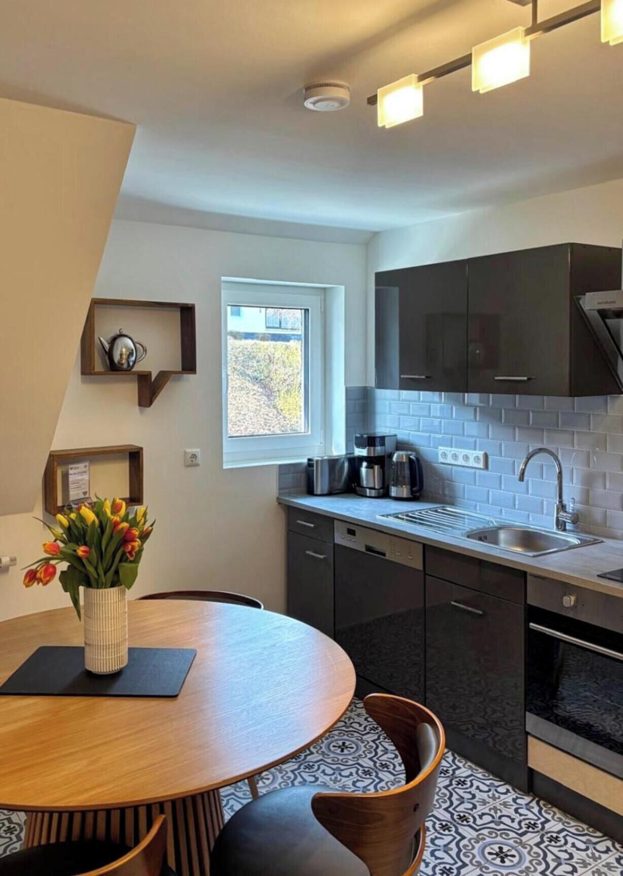 A modern kitchen with dark cabinets, a built-in oven, and a window.
