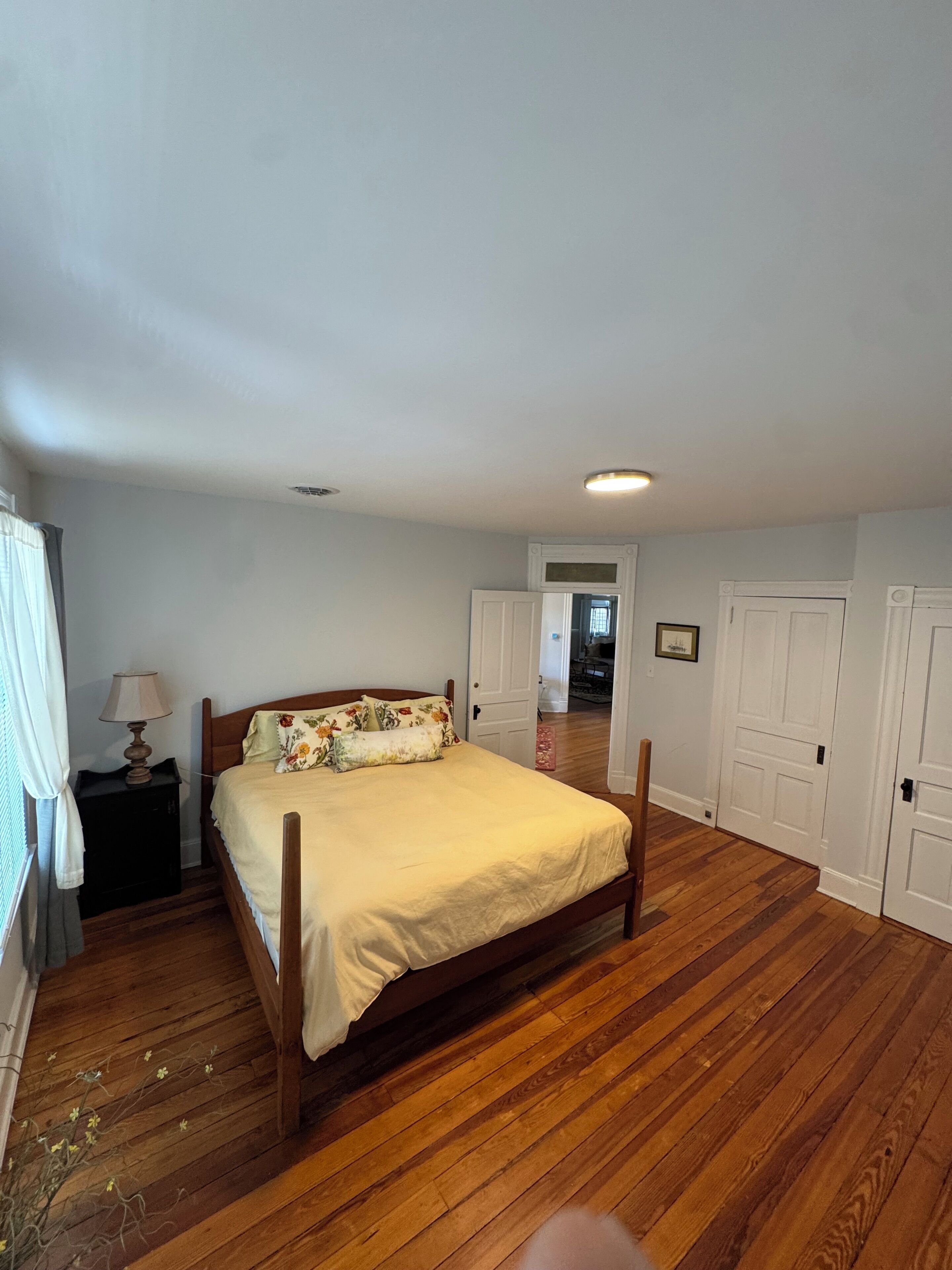 Un dormitorio con una cama de madera, una mesita de noche, una lámpara y una puerta que da a otra habitación.