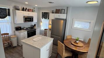 A modern kitchen with white cabinetry, a central island, and a dining area with wicker chairs.
