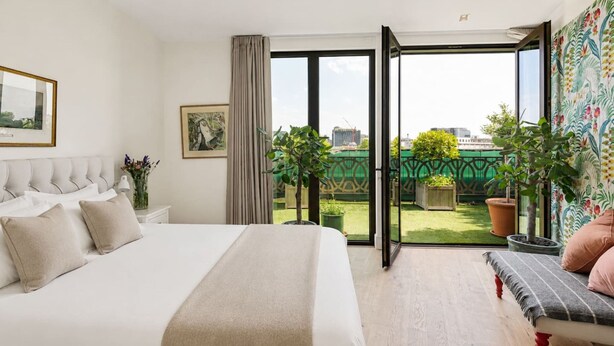 Een hotelkamer met een bed, een bankje, uitzicht op de stad en potplanten.