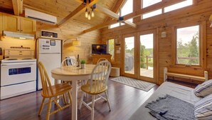 A wooden cabin interior with a kitchen, dining area, and living room, featuring a large window and a TV.