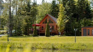 A cabin with a deck, surrounded by trees and a pond.