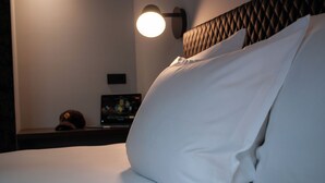 A hotel room with a bed, pillows, a headboard, a wall-mounted lamp, and a television on a stand. - gambino hotel GOETHE26 (Munich)
