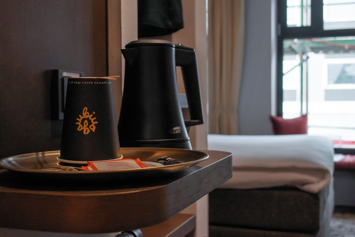 A hotel room with a coffee maker, a tray with a cup and a packet, and a bed with a pillow.
