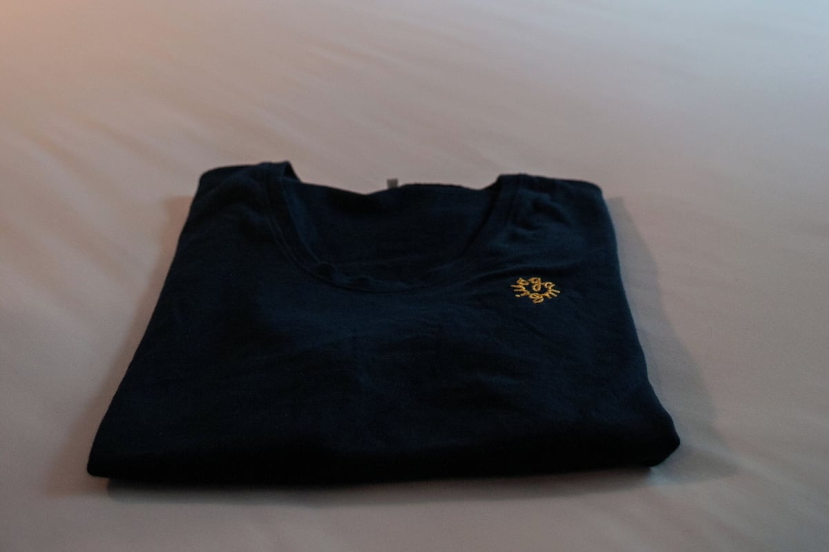 A neatly made bed with white linens, a dark blue shirt on the bed, and a hanging light fixture in the background.