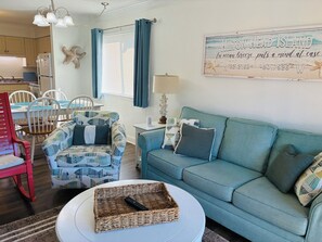 Een woonkamer met een blauwe bank, een gestreept fauteuil en een ronde salontafel met een mand.