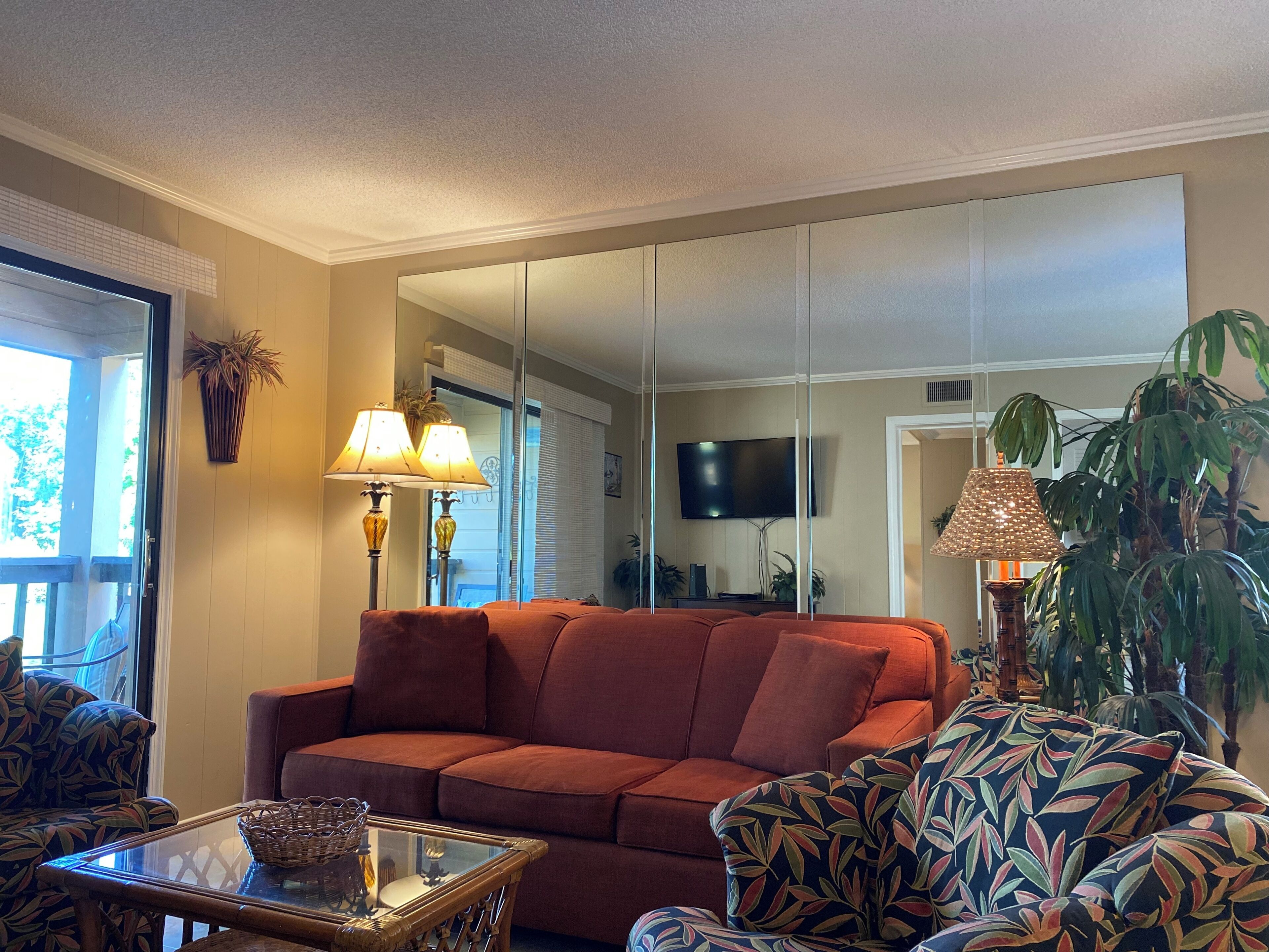 A living room with a sofa, a glass coffee table, a TV, and a large mirror.