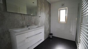 Une salle de bain moderne avec un meuble-lavabo blanc, un miroir, une petite fenêtre et un espace douche.
