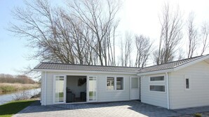 Une maison de plain-pied dotée d’un patio couvert, d’une porte donnant sur un espace intérieur et offrant une vue sur une étendue d’eau.