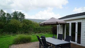 Une terrasse avec une table et des chaises, un parasol, et une maison avec une porte de garage.