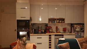 Uma cozinha compacta com armários brancos, forno embutido, máquina de café e lava-louças.