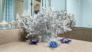Un acquario con barriera corallina dotato di pareti in vetro, un piano di lavoro in granito e un bagno con tenda da doccia blu sullo sfondo.