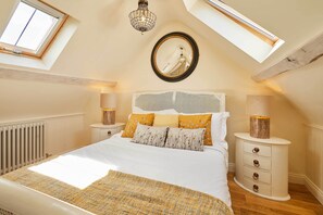 A bedroom with a skylight, a bed with patterned bedding, a bedside table with lamps, and a mirror on the wall. - Host & Stay | Topsail (Whitby)