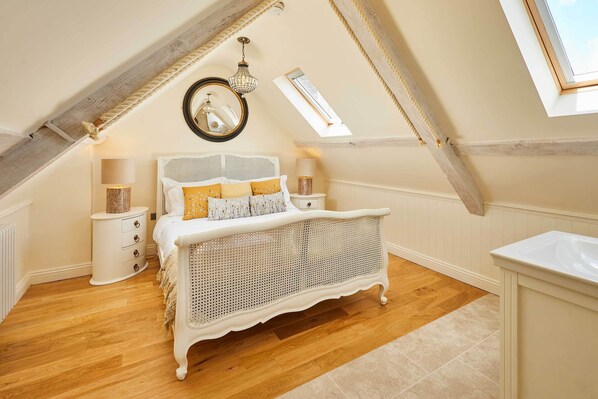 A bedroom with a sloped ceiling, a bed with a woven headboard, bedside lamps, and a large mirror. - Host & Stay | Topsail (Whitby)