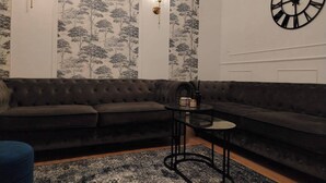 Ein Wohnzimmer mit einem dunkelbraunen Sofa, einem Glastisch und einer großen Wanduhr.