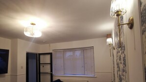 Ein Wohnzimmer mit einem dunklen Sofa, einem Glastisch, einem Fernseher und einer Kristallleuchter.