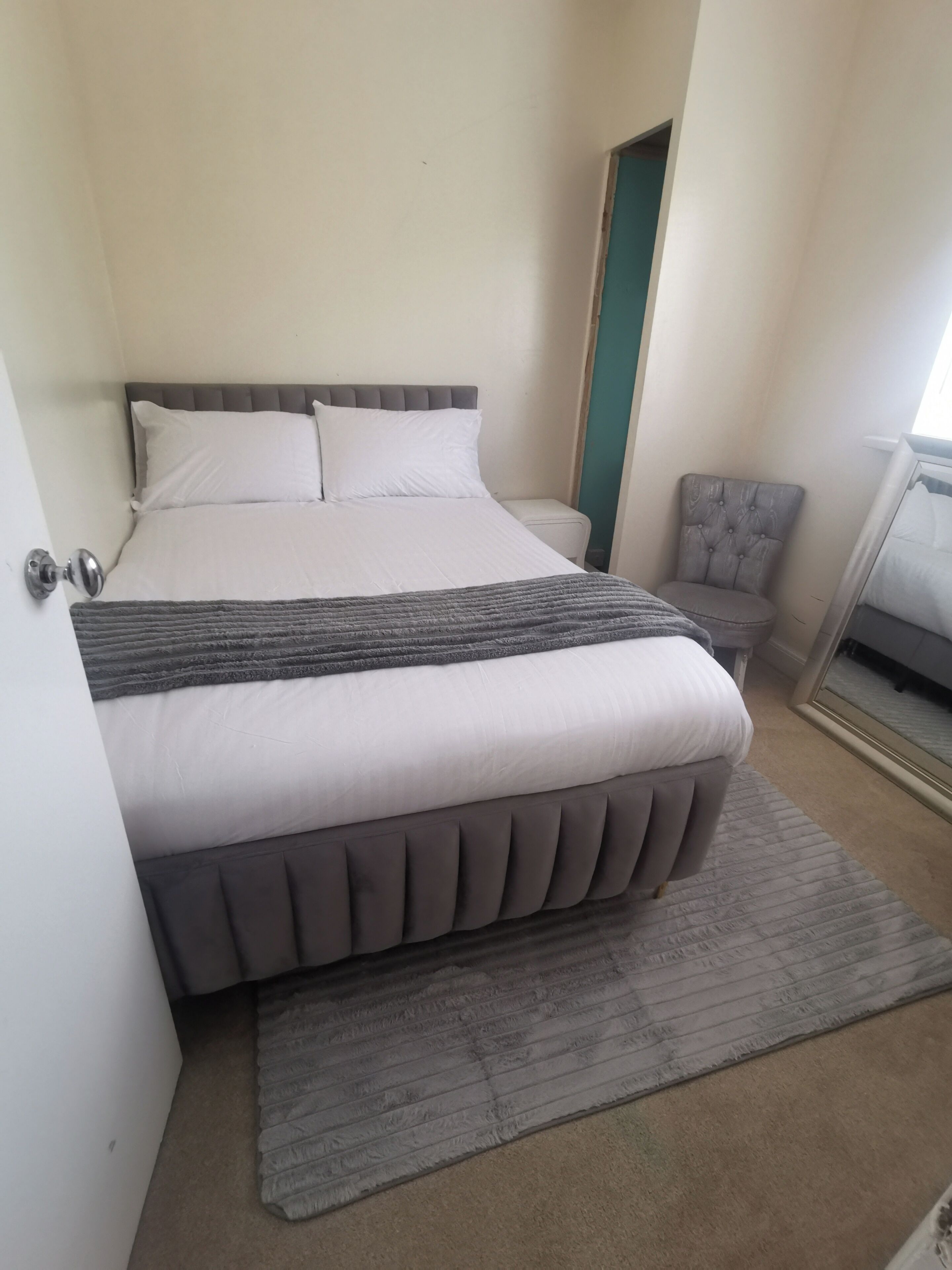 Un dormitorio con cama, una silla, un espejo y una puerta.