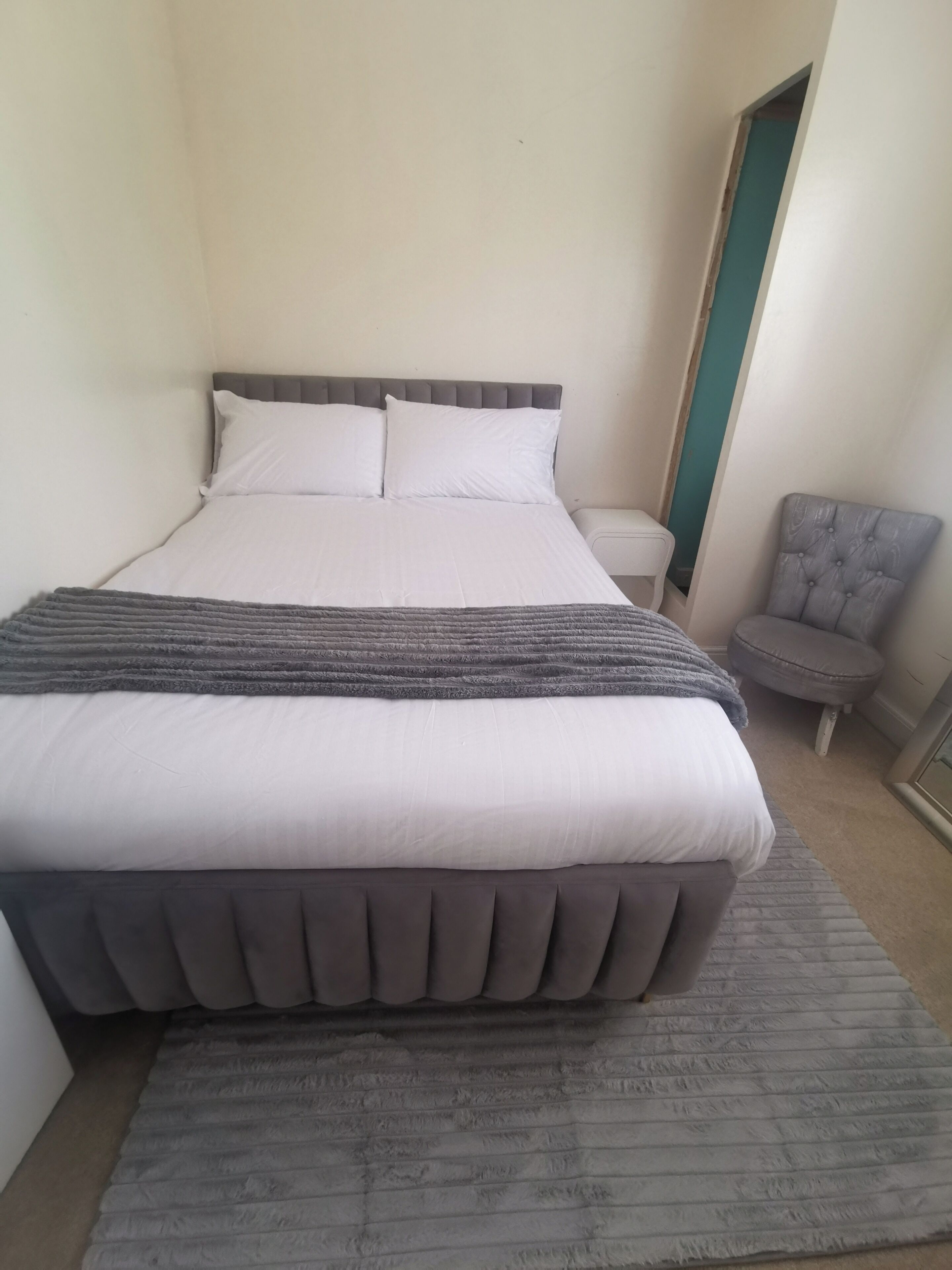 Una cama bien hecha con cabecera y piecera grises, una manta gris y una alfombra gris en el suelo.
