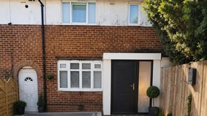 Ein Wohnweg führt zu einem Haus mit einer schwarzen Tür, einer weißen Tür und einem Fenster mit Rollläden.