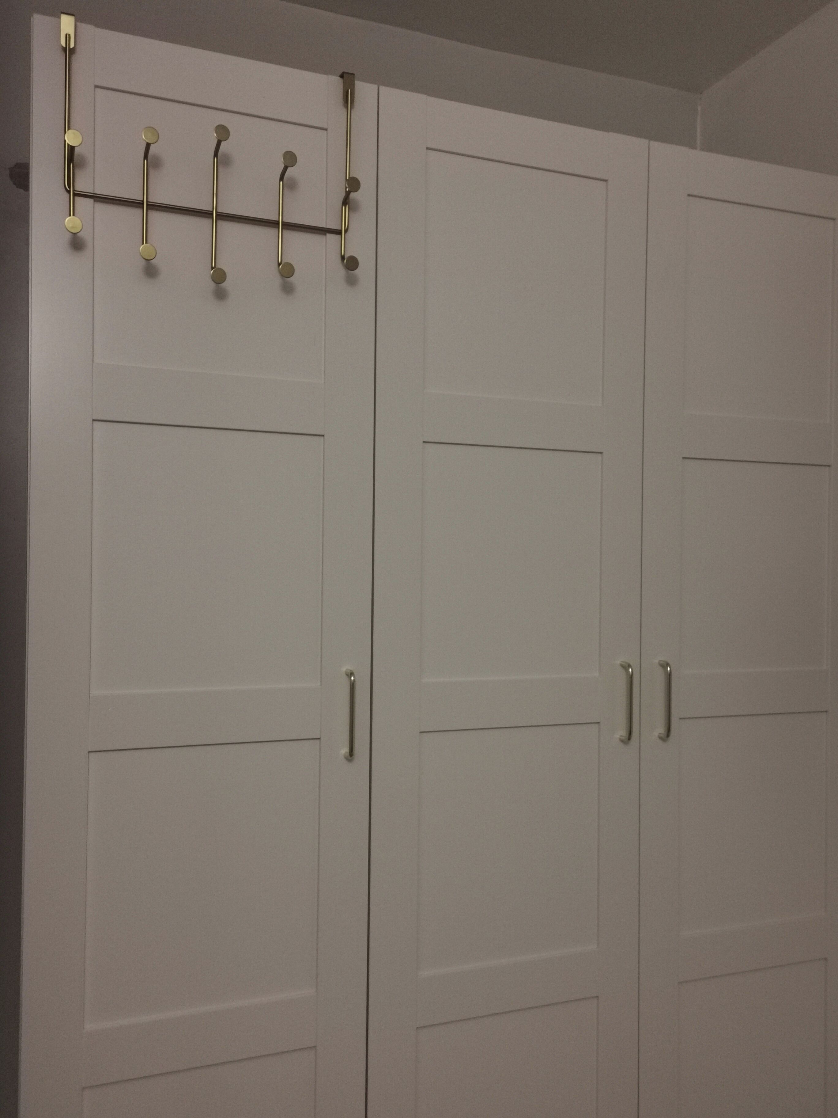 A set of white double doors with a metal handle and a horizontal bar with circular hooks.