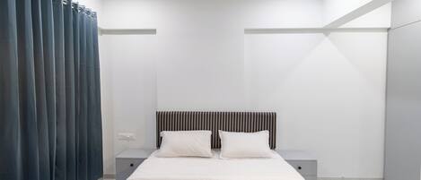 Un dormitorio moderno con cama, dos mesitas de noche, cabecero y cortina.