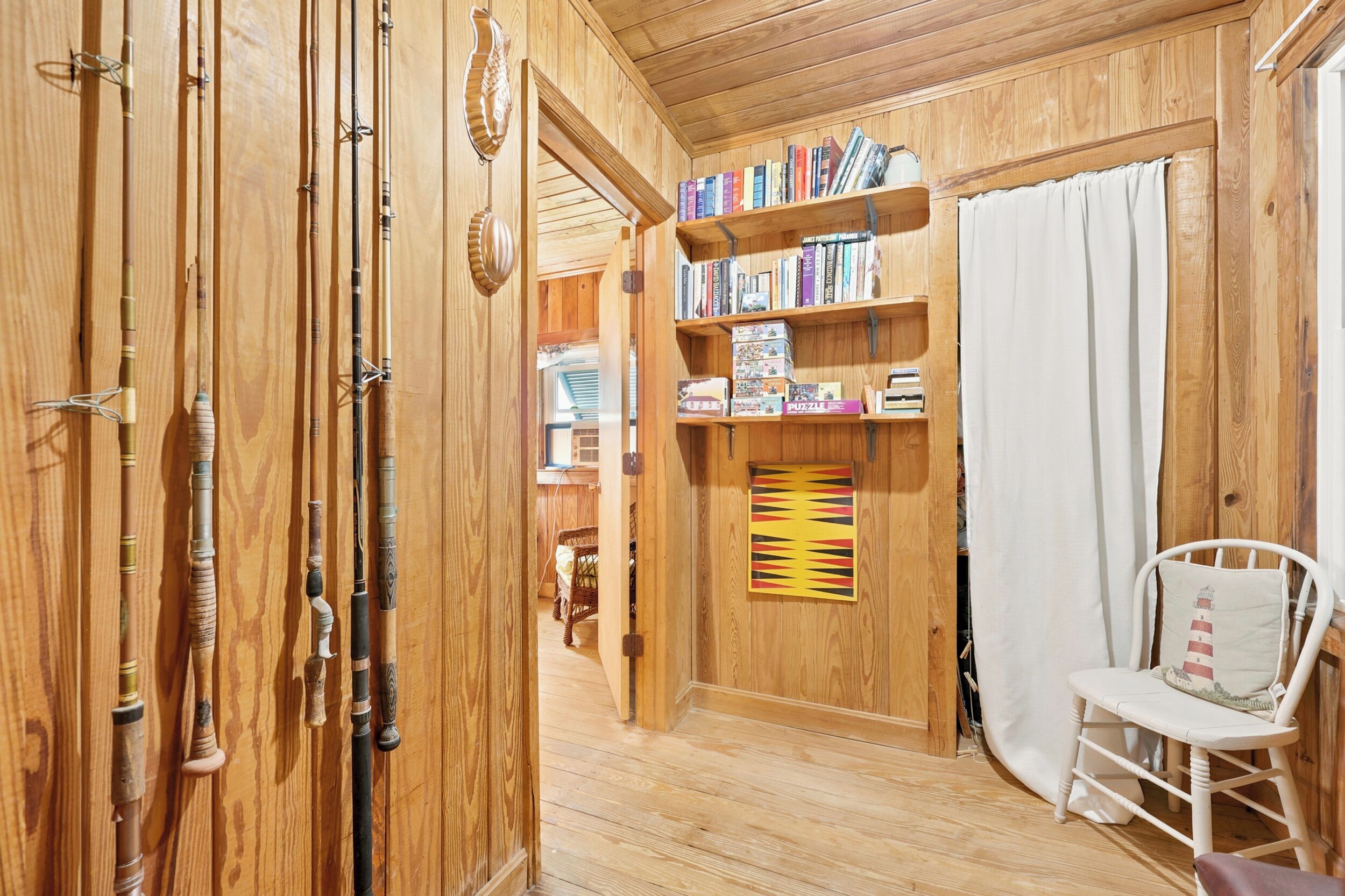 A wooden interior with a bookshelf, a chair, and a door with fishing rods.