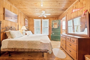 A wooden cabin bedroom with a bed, dresser, and a ceiling fan. - Fiddlers Roost - Creek Front - 4 Bedrooms (Pawleys Island)