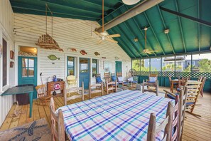 A covered outdoor dining area with wooden tables and chairs, a ceiling fan, and a view of the surrounding area. - Fiddlers Roost - Creek Front - 4 Bedrooms (Pawleys Island)