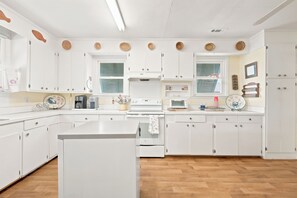 A modern kitchen with white cabinets, a central island, and a microwave. - Fiddlers Roost - Creek Front - 4 Bedrooms (Pawleys Island)