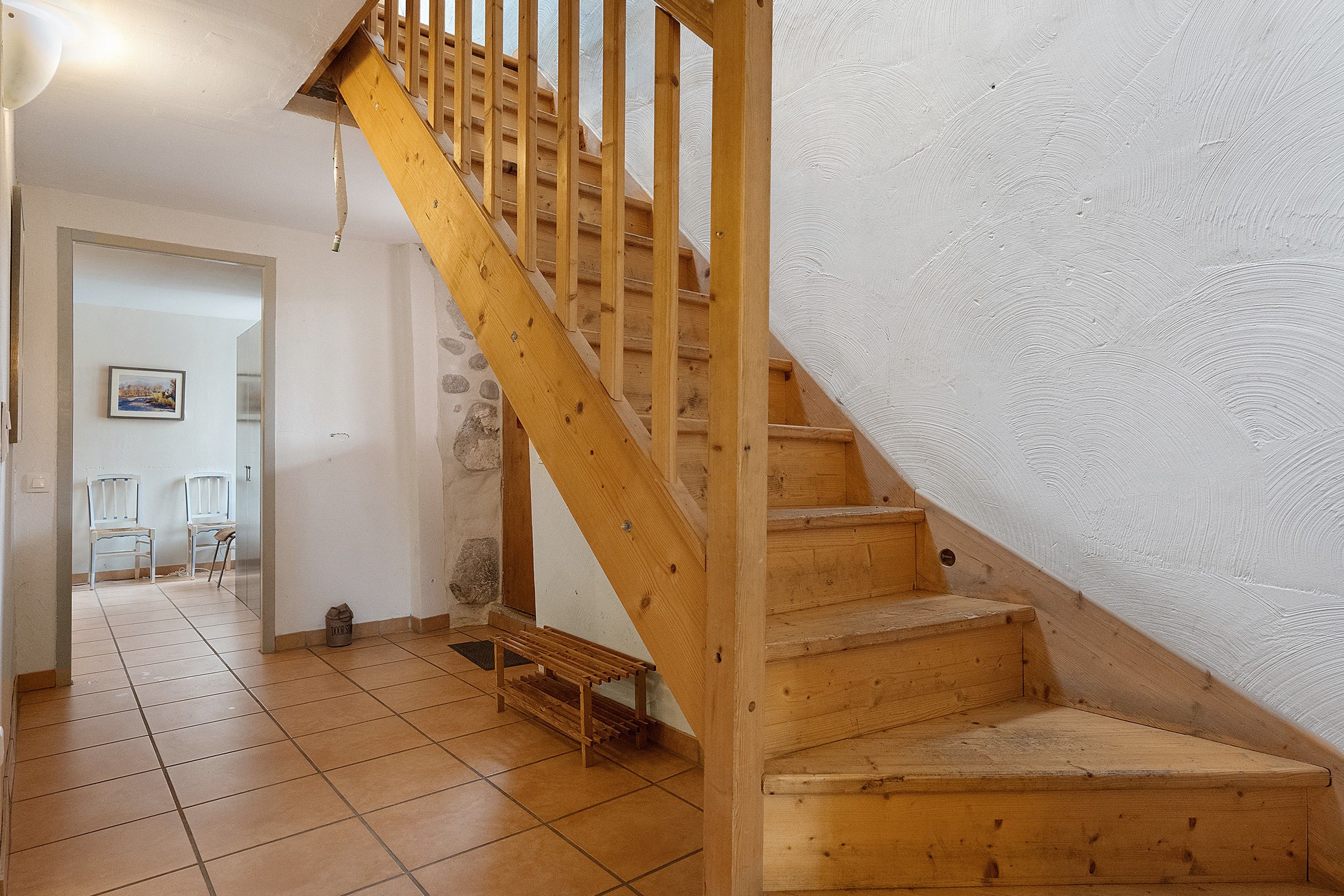 Una escalera de madera que lleva a un rellano con suelo de baldosas y una puerta que da a otra habitación.