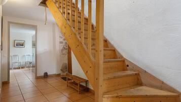 Una escalera de madera que lleva a un rellano con suelo de baldosas y una puerta que da a otra habitación.