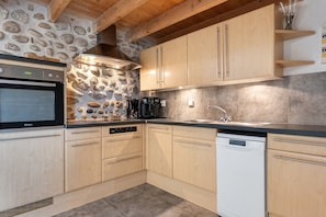 Una cocina con armarios de madera, horno empotrado, cafetera y salpicadero de pared de piedra.