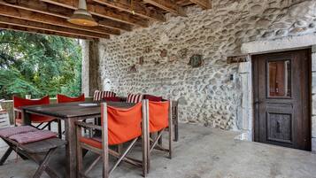 Un espace extérieur aménagé pour les repas, avec un mur en pierre, des meubles en bois et une porte.