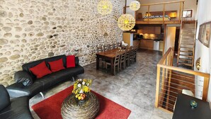 A living room with a stone wall, a sofa, a dining table, and a staircase. - Country House “Gîte Noisettes” with Shared Pool, Private Terrace, and Wi-Fi (Saint-Didier-sous-Aubenas)