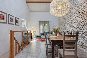 A dining area with a wooden table and chairs, a stone wall, and a staircase leading to another level.